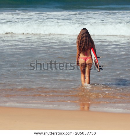 Rear view of beautiful sexy young woman surfer girl in bikini with white surfboard on a beach
