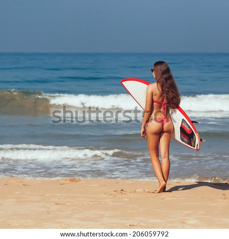 Rear view of beautiful sexy young woman surfer girl in bikini with white surfboard on a beach
