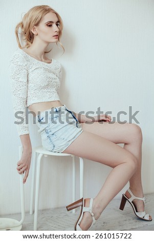 fashion model in white top and jeans posing sitting on chair posing over white background