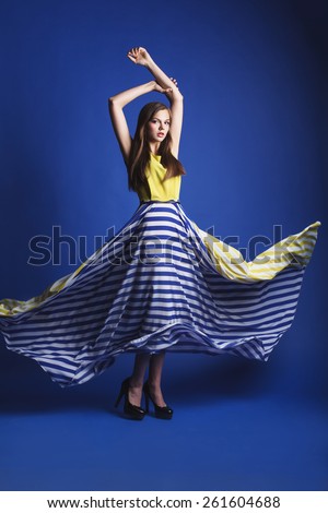 beautiful woman in long yellow blue dress posing dynamic in the blue background