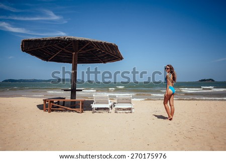 Woman resting on a tropical beach near deck chair and sun umbrella. Blue sky, deserted beach