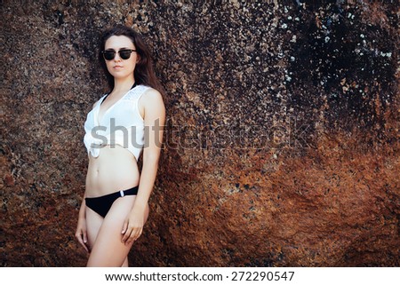 Young girl in black swimsuit and white  blouse on the rocks near the sea beach.