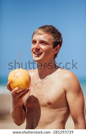 attractive man drinks coconut juice from a nut on a beach at the ocean