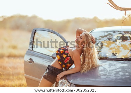 happy young woman with car - sexy rich lady driver with long blond healthy hair at automobile .summer portrait . beautiful slim fashion girl posing near car