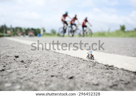 An old man  (miniature) on cycle ride in country road with a group of bicycle race background.Soft focus and shallow depth of field composition with soft pastel color.