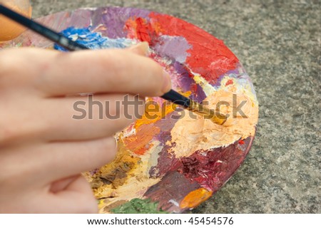 hand holding paintbrush and mixing oil-paint on palette