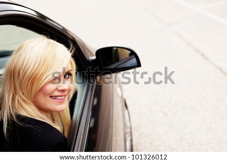 Pretty blonde gives a big smile from the passenger side of a modern automobile.