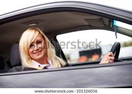 Pretty woman driver seated behind the wheel of a saloon car looking down out of her window
