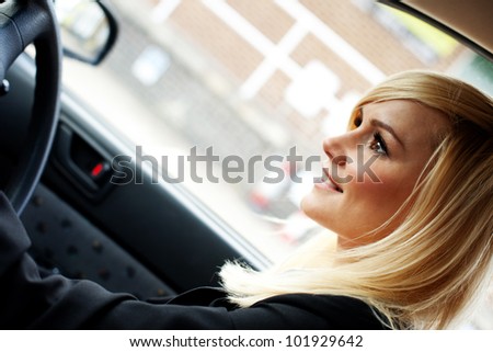 Beautiful businesswoman seated behind the steering wheel driving a ca in an urban environmentr