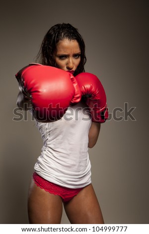 Athletic woman boxer wearing red leather boxing gloves wet with perspiration throwing a punch at the camera