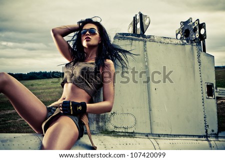 Artistic portrait of sexy slender long-legged woman in skimpy two piece outfit sitting on the fuselage of an abandoned old plane on a stortmy day