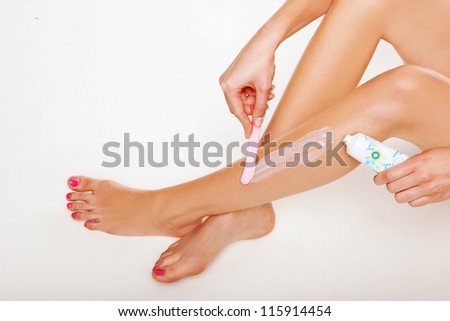 Woman applying depilatory cream with a spatula to her shapely sexy legs to remove any surface hair