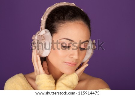 Elegant woman wearing ear muffs to guard against the winter cold on a purple studio background