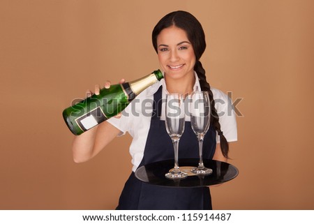 Beautiful waitress pouring champagne into two elegant flutes that she is balancing on a tray