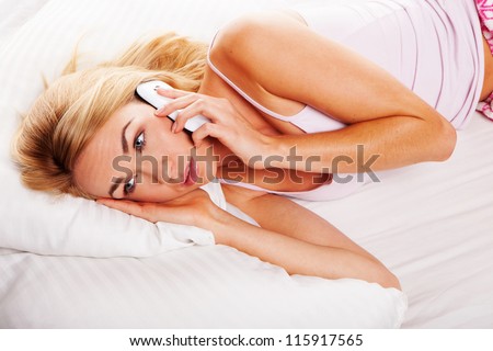 Pretty blonde woman lying in her bed listening to a conversation on her mobile with wide open eyes