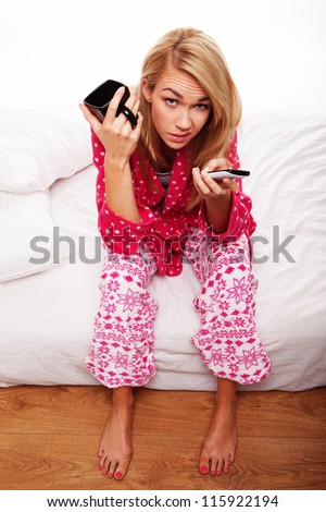 Disgruntled young woman in her pyjamas sitting on the edge of her bed changing TV channels