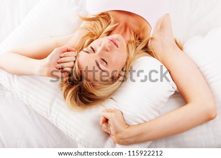Beautiful sleepy young woman stretching her arms as she lies in bed trying to wake up