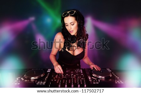 Glamorous sexy busty DJ at work mixing sound on her decks at a party or night club with colourful strobe light background