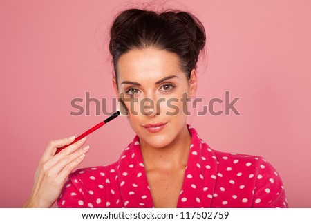 Glamorous woman applying blusher with a large soft bristle cosmetics brush to contour her cheekbones