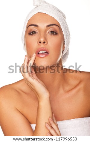 Beautiful graceful woman with her head wrapped in a towel applying lip gloss with the tip of her finger isolated on white