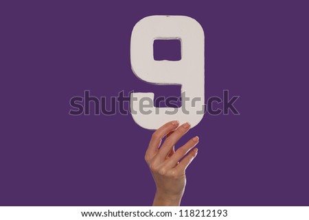 Female hand holding up the number nine against a purple background conceptual of numbers, measurement, amount, quantity, accounting and mathematics