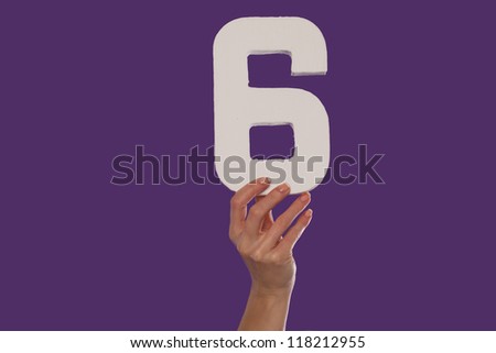 Female hand holding up the number 6 against a purple background conceptual of numbers, measurement, amount, quantity, accounting and mathematics