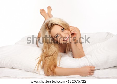 Happy blonde woman relaxing on a lovely thick soft duvet in lingerie smiling at the camera while holding back her long blonde hair