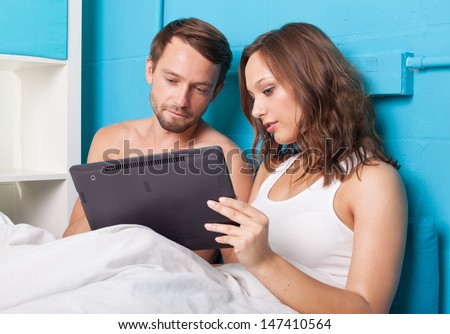 Young couple browsing internet on tablet computer while sitting in bed
