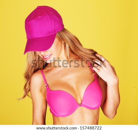 Trendy young woman with long blond hair dancing in a pink bikini and matching peaked cap with a smile of pleasure on her face against a yellow background