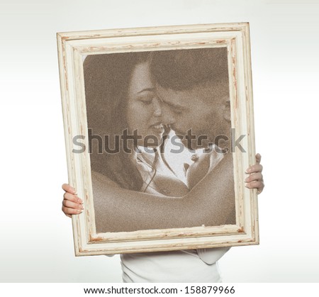 Woman holding a romantic sepia toned picture of a couple in love with their foreheads touching so that it conceals her face and upper body, isolated on white