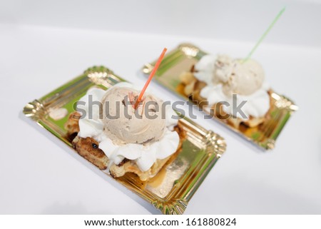 Two desserts on metallic trays with ice cream and cream topping a waffle or layer of cake, high angle view