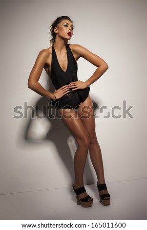 Seductive young woman with her brunette hair in a ponytail in black lingerie posing in high heels with her leg raised giving the camera a sultry provocative look