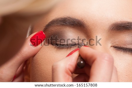 Close up view of the eye of a young female model having eye makeup applied by a beautician