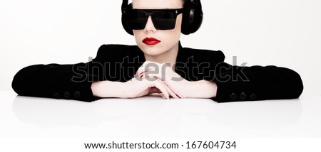 Dramatic portrait of a sexy woman in sunglasses listening to music on a set of headphones leaning on a table looking at the camera