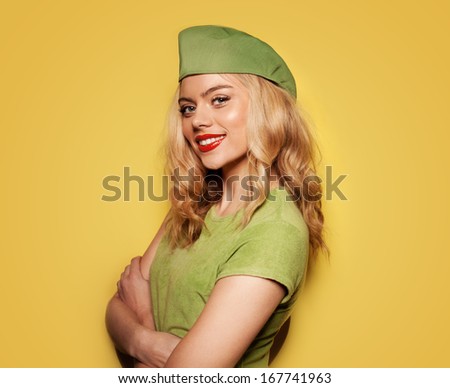 Beautiful glamorous blond woman in a trendy green summer ensemble standing with folded arms and a jaunty expression on yellow