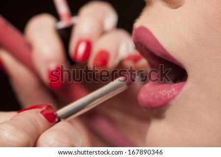 Closeup of the fingers of a female beautician or makeup artist applying lipstick to the lips of a model