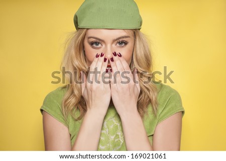 Beautiful woman with long blond hair wearing a chic green outfit showing off her manicured nails on a yellow background