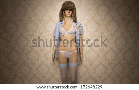 Store mannequin dressed in blue and pink lingerie wearing a furry winter cap and unbuttoned shirt against vintage wallpaper with vignetting