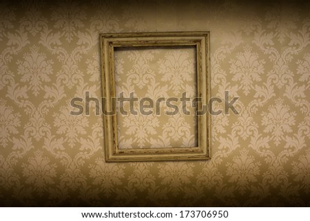 Empty wooden antique picture frame hanging on retro beige wallpaper with an arabesque pattern with vignetting on the top and bottom borders of the frame