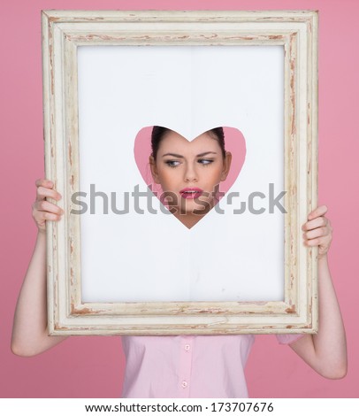 Beautiful young woman with her face framed by a heart as she looks through a cut out heart shape in an old vintage picture frame while posing for her sweetheart for Valentines Day