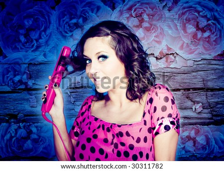 beauty brunette girl standing with a pink hair straightener and polka dots top . smiling