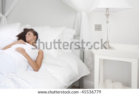 Beautiful young brunette woman sleeping in her white bedroom
