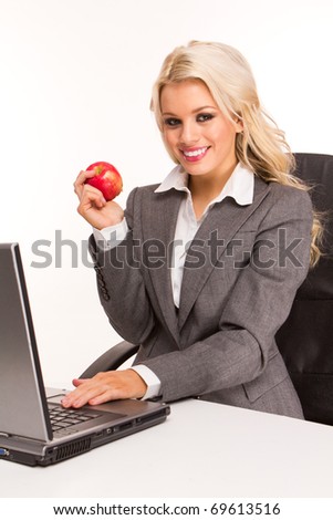 Portrait of an sexy business woman sitting by a desk and laptop eating red apple for a breakfast