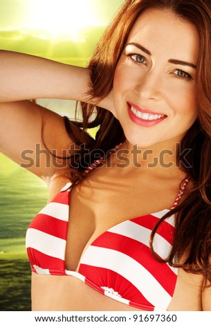 Beautiful smiling woman with auburn hair wearing a red and white striped bikini, outdoors against greenery