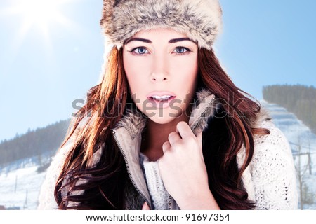 Winter Woman On Ski Slope. Close-up head-shot of a beautiful woman dressed in winter fur with a mountain ski slope background