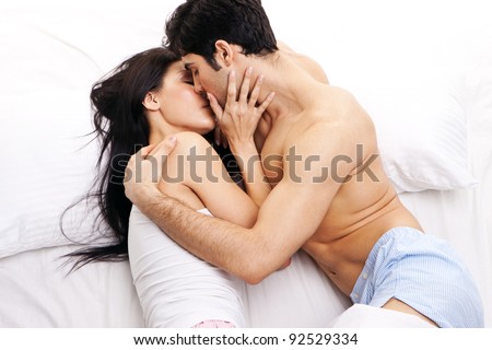 An attractive young couple in a loving embrace kissing one another in bed.