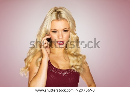 Stunning woman with long wavy blonde hair using a mobile phone on maroon studio background