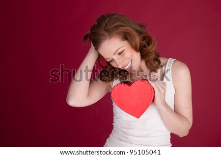 Laughing attractive woman holding a red heart-shaped gift box to her chest.