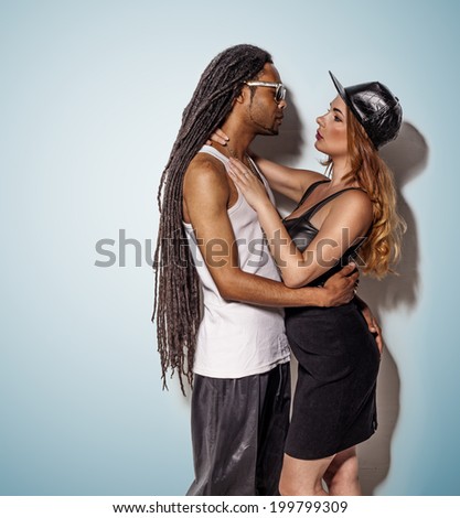 young multiracial couple with a dreadlock African American man wearing sunglasses and cute blond woman wearing dress against the wall kissing