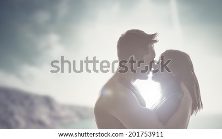 Loving young couple enjoying a romantic kiss backlit by the sun with flare effect and a mountain background